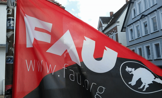Ein sich bewegendes Gif einer wehenden Fahne der FAU. Diese ist rot-schwarz mit den Aufschriften "FAU" und "www.fau.org" und einer weißen anarchosyndikalistischen Katze daneben.